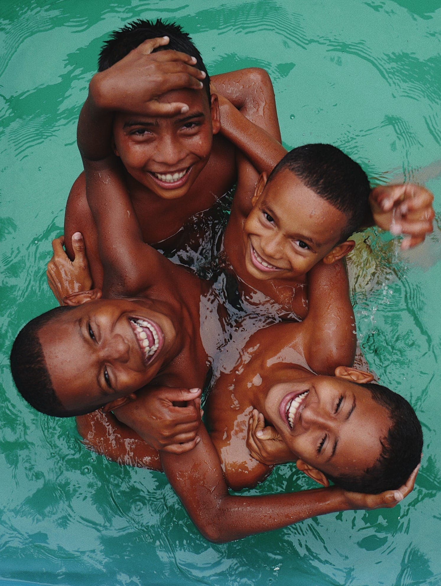 Quatro meninos sorrindo abraçados na água