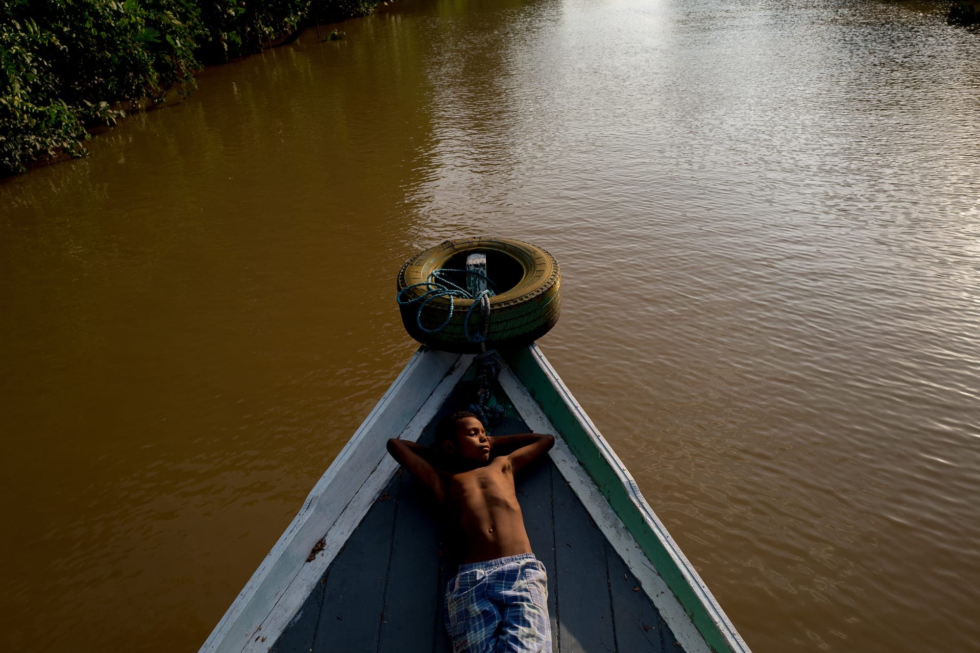 Menino deitado na proa de uma canoa no rio