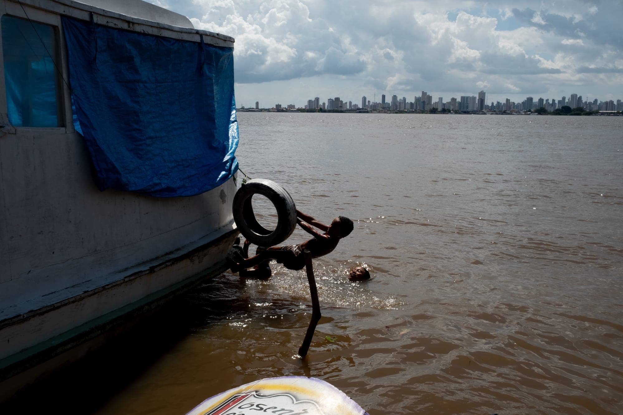 Casco de barco e pneu na água, com a cidade ao fundo
