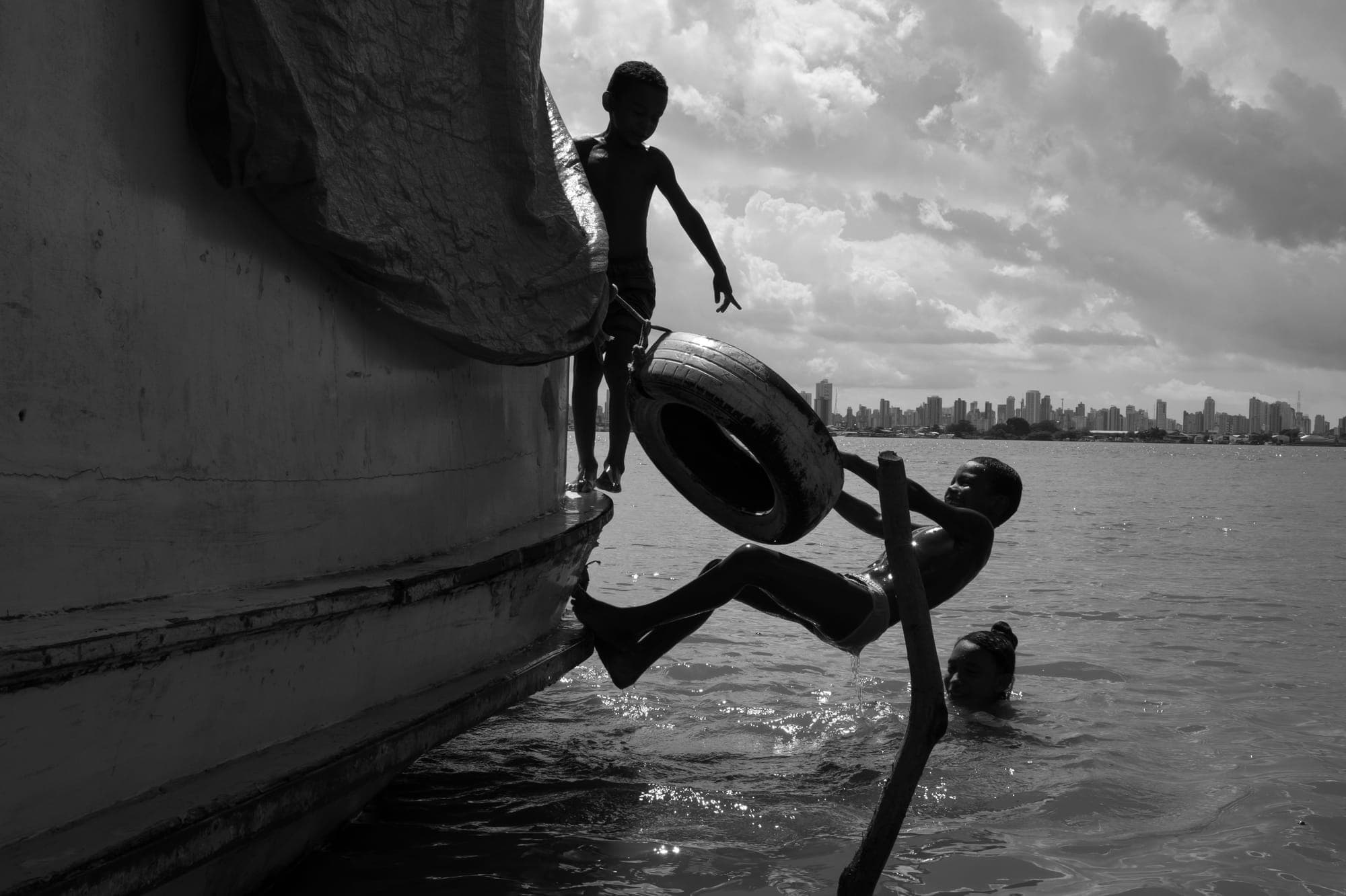 Criança salta de um barco para o rio, em preto e branco
