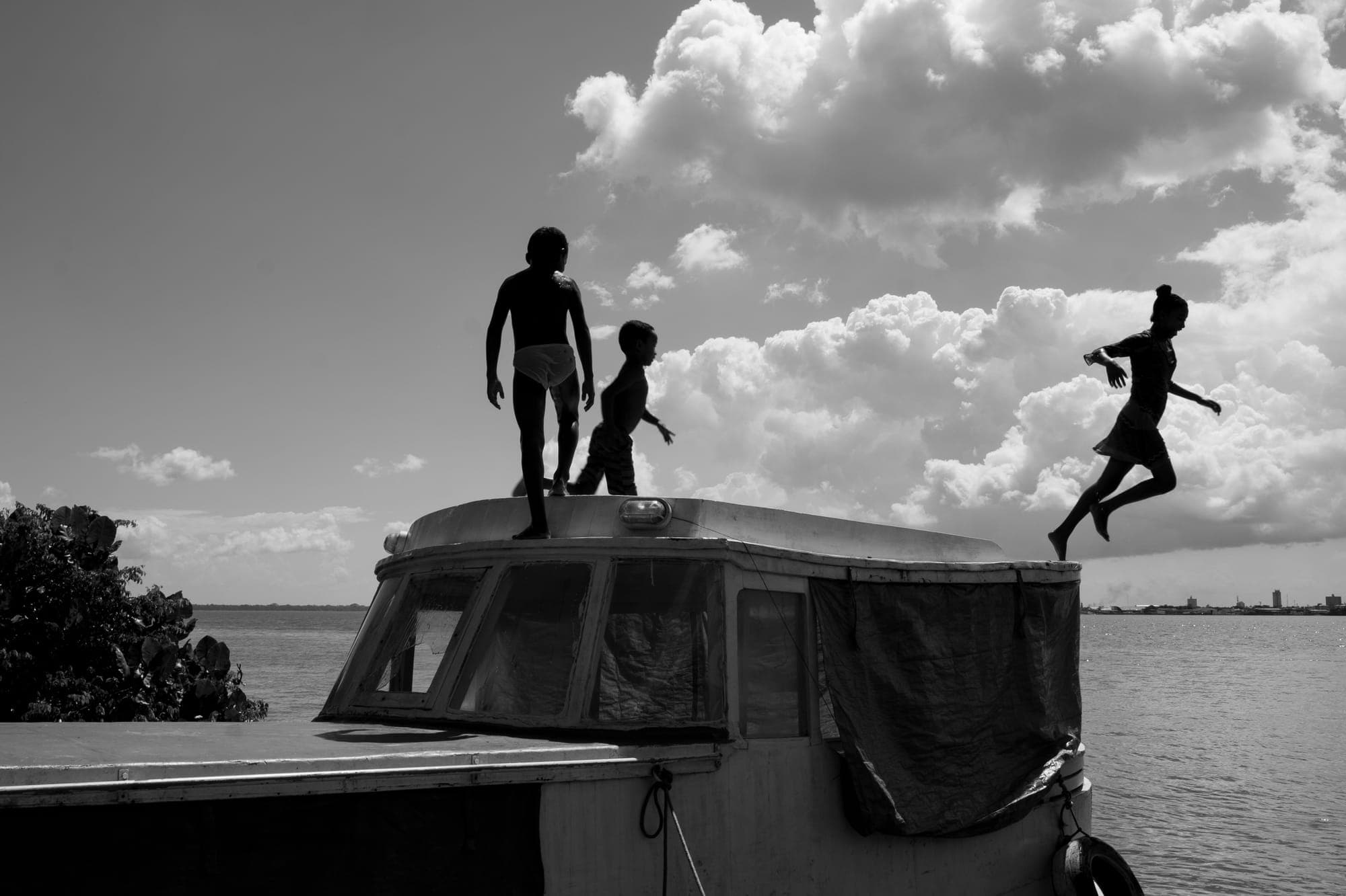 Crianças saltam do teto de um barco, em preto e branco