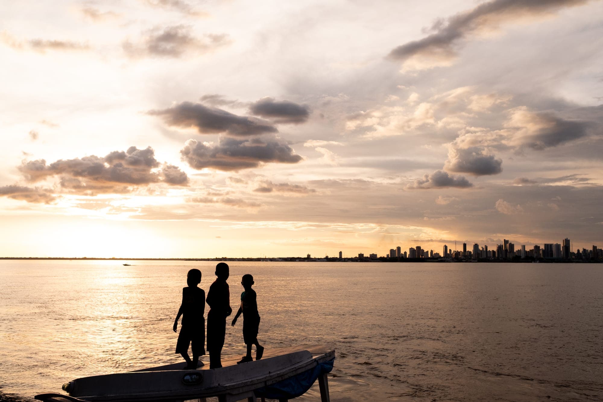 Silhuetas de três crianças em uma canoa ao pôr do sol