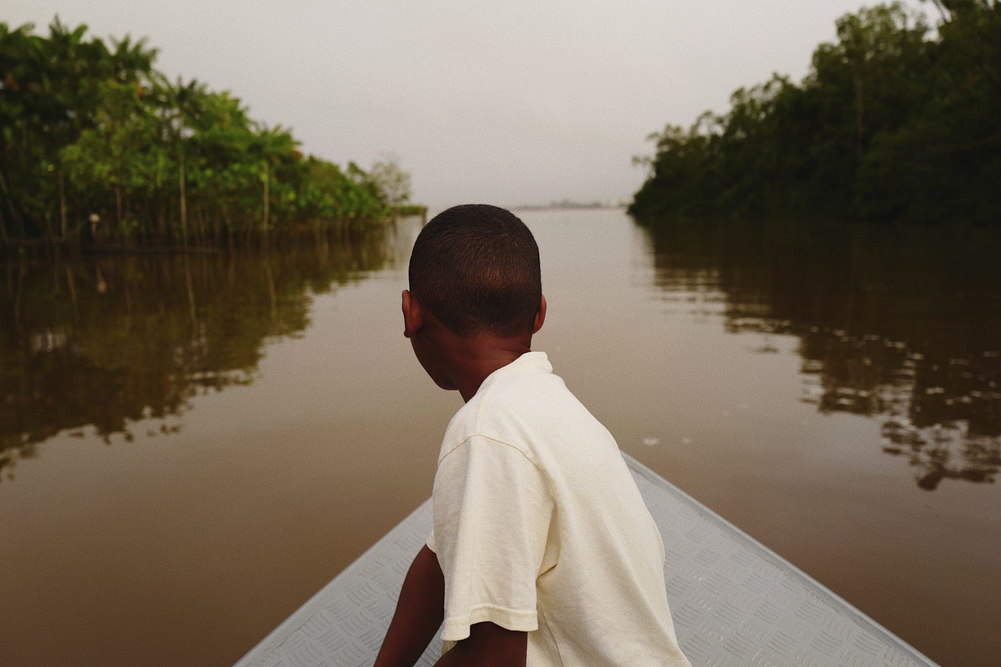 Menino na proa de uma canoa olhando o rio