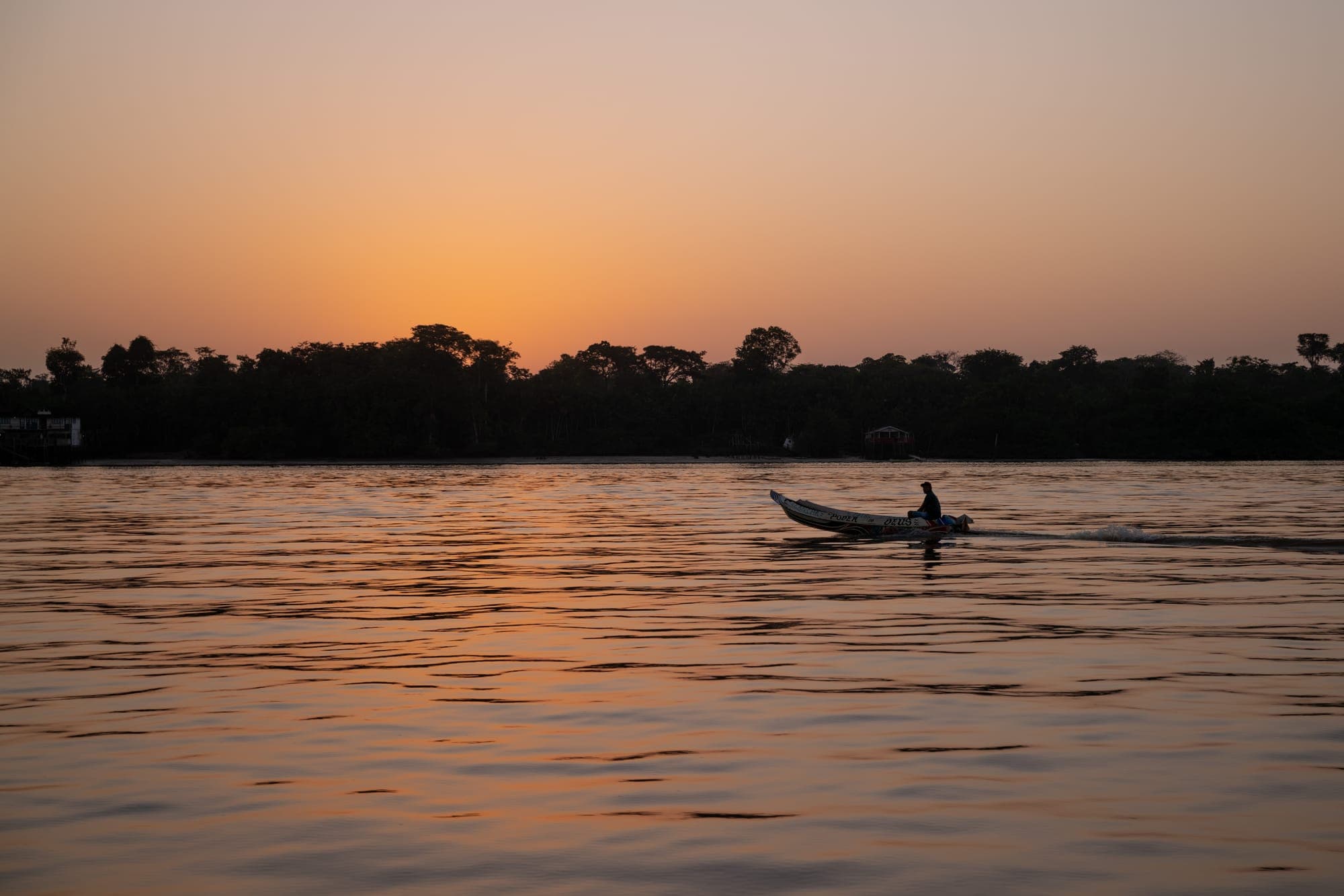 Canoa atravessa o rio ao pôr do sol