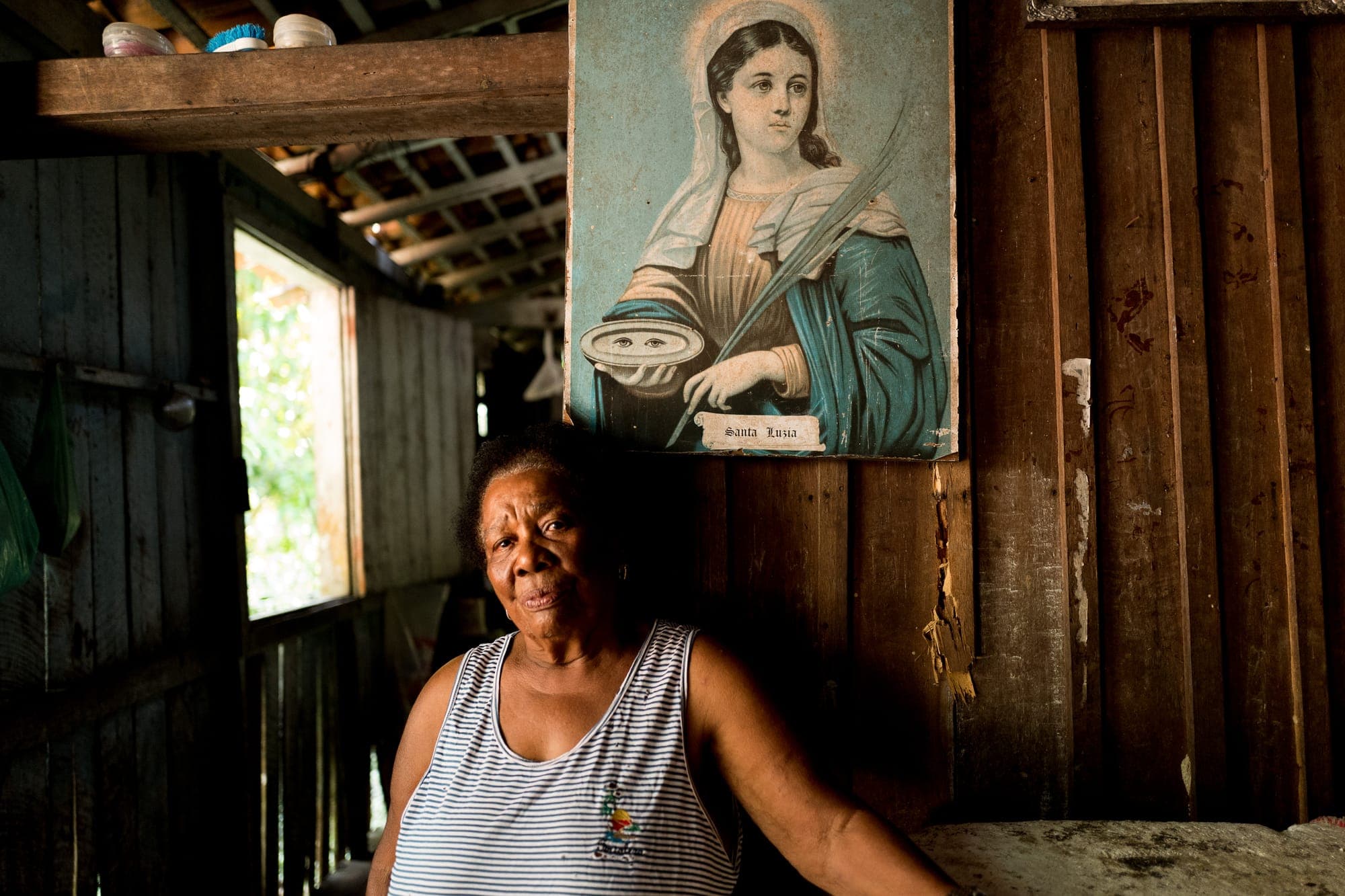 Moradora sentada em casa sob um quadro de santa