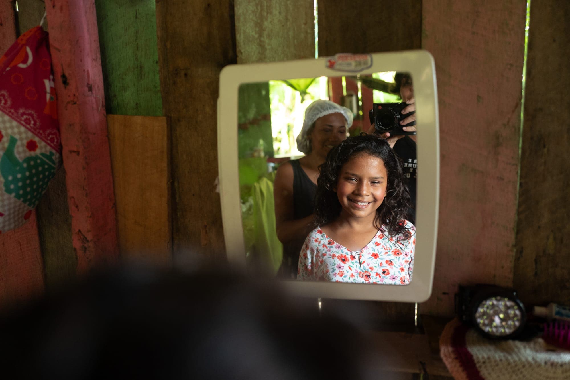 Menina sorri refletida em um espelho na parede