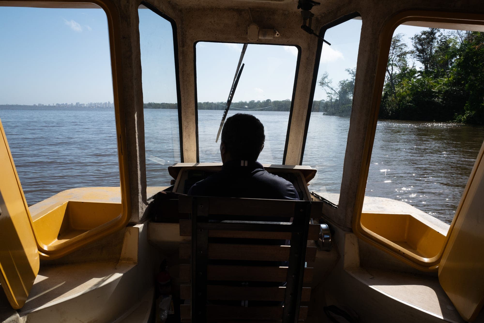 Homem pilota um barco, visto por trás, com o rio adiante