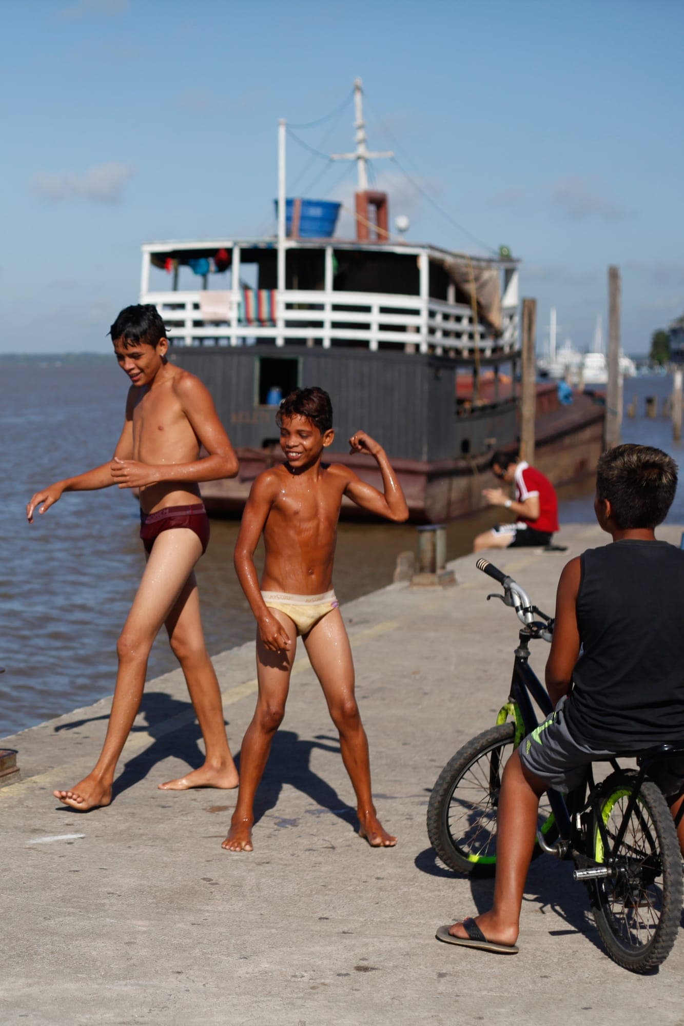 Meninos na beira do rio diante de um barco grande