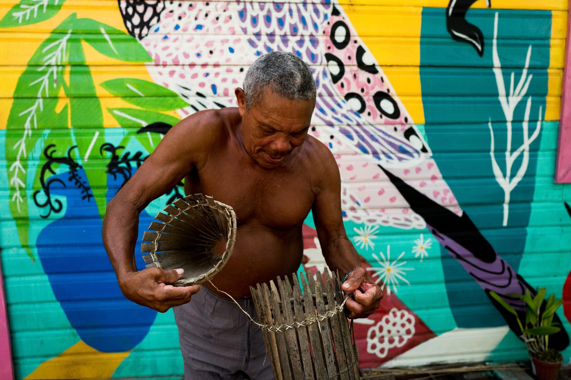 Pescador segura um paneiro diante de um mural colorido