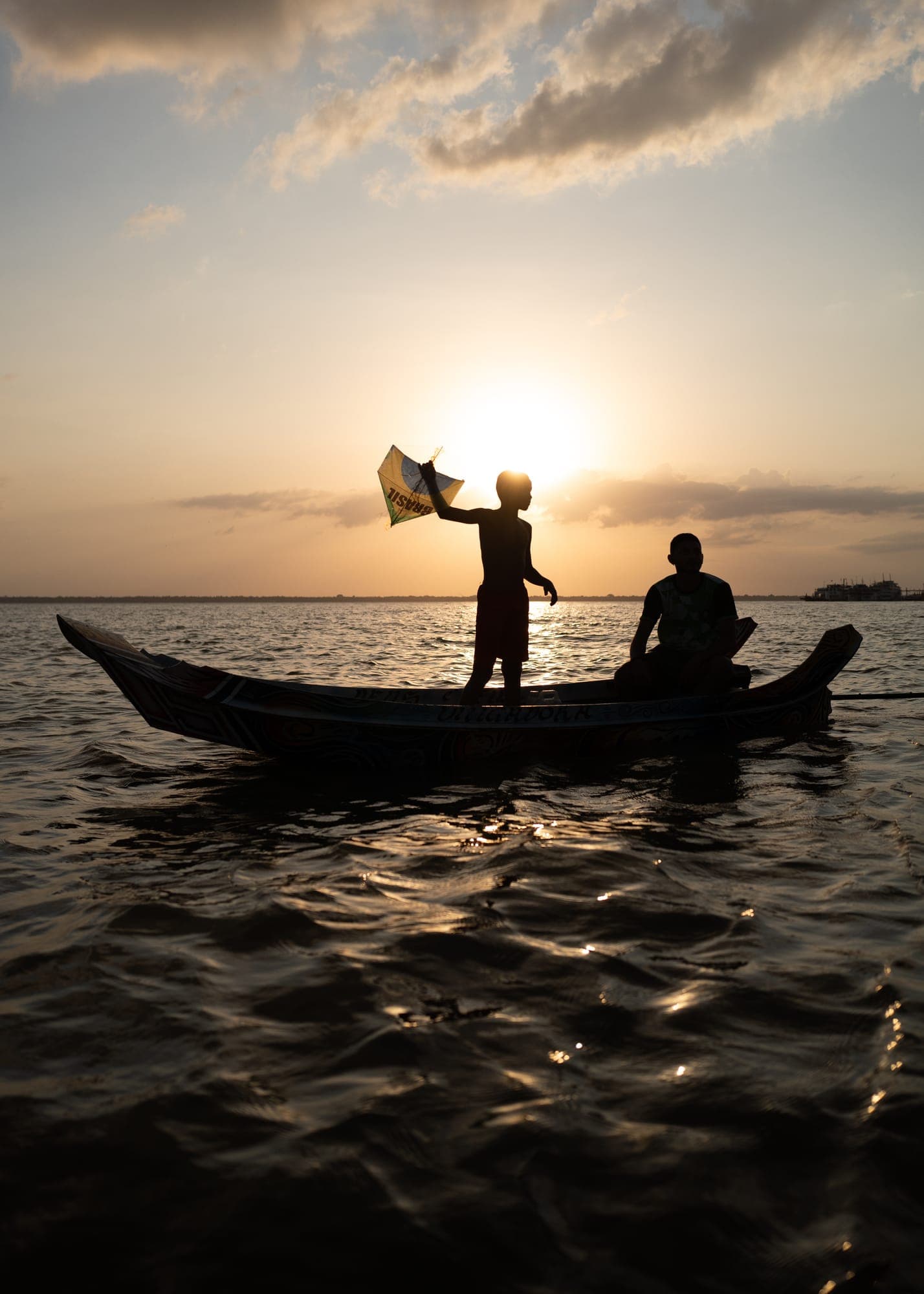 Silhuetas de pescadores jogando a rede de uma canoa ao pôr do sol