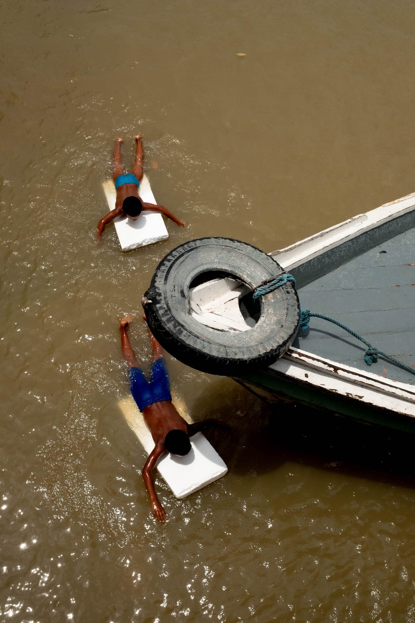 Crianças com pranchas na água ao lado de um barco, vistas do alto
