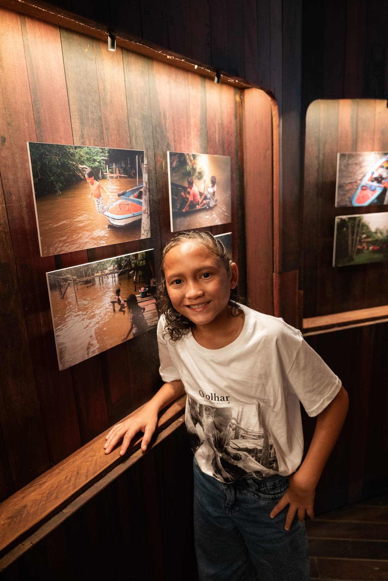 Menina sorri ao lado de suas fotografias na galeria
