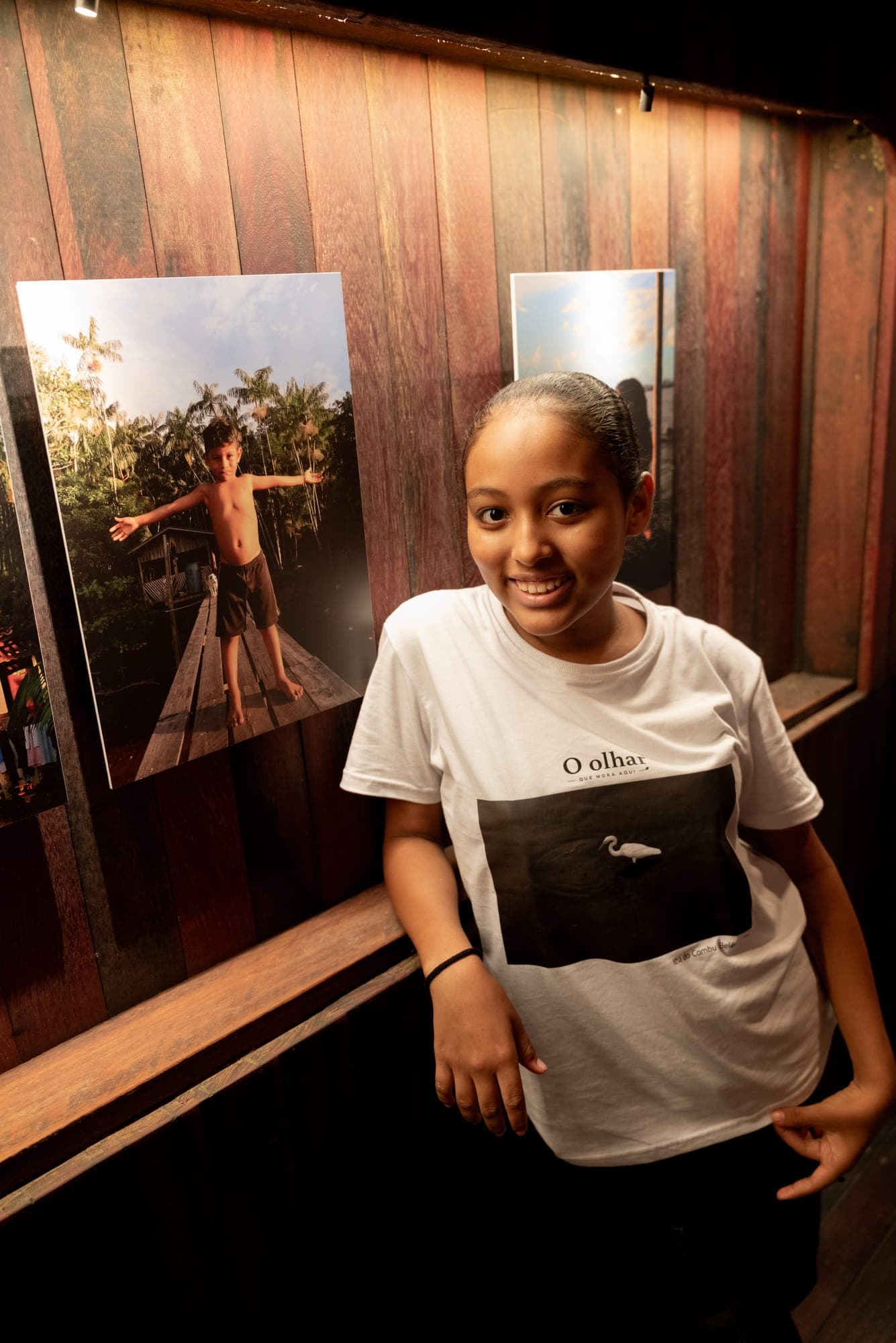 Menina sorri ao lado de sua fotografia exposta