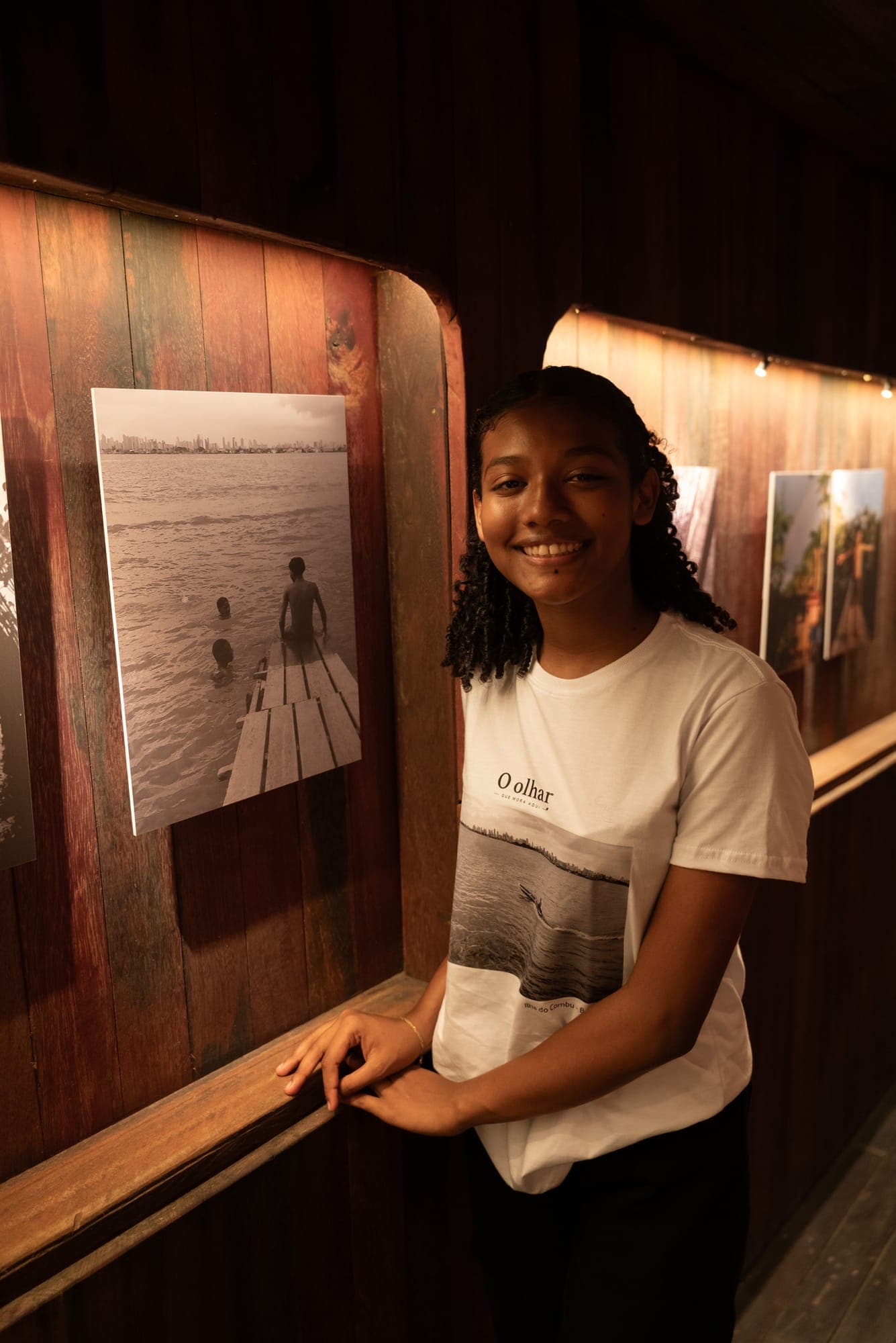 Menina sorri ao lado de sua fotografia exposta