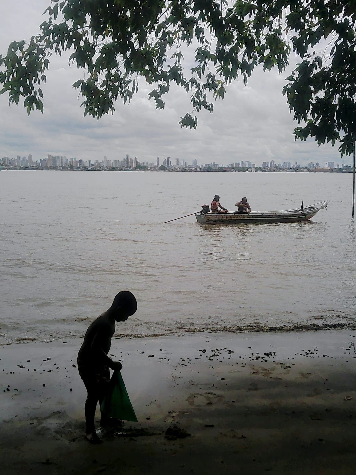 Criança na beira do rio com uma canoa ao fundo