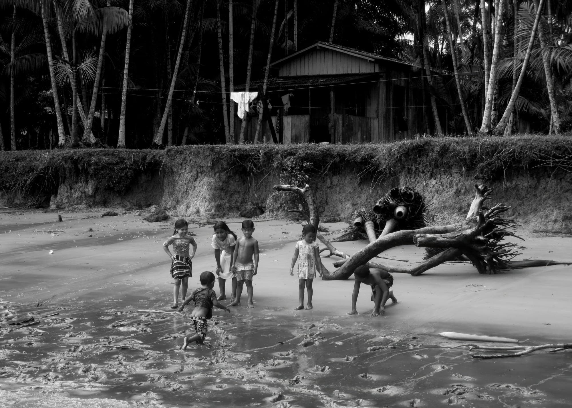 Crianças brincam na areia da beira do rio, em preto e branco