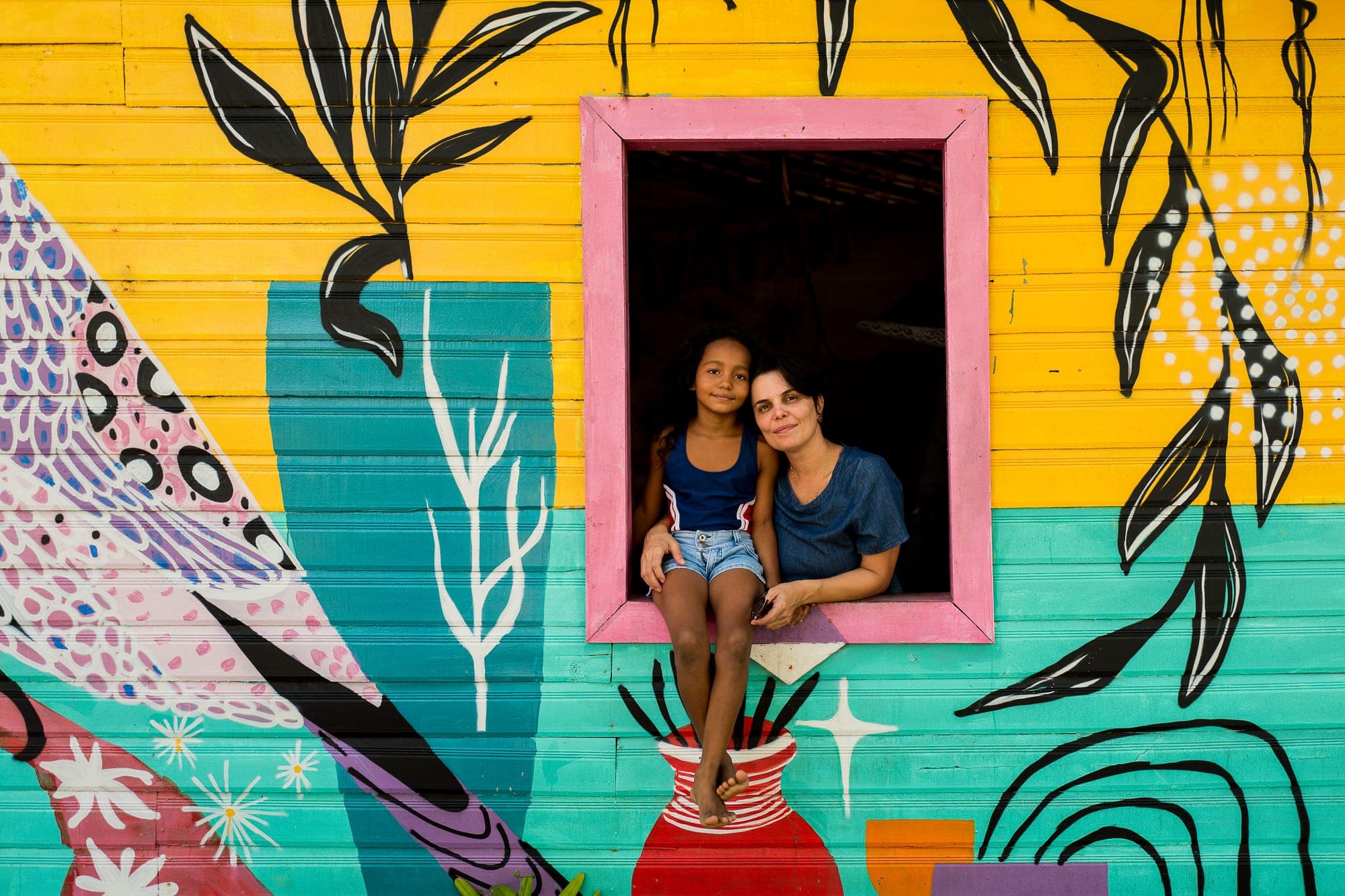 Duas meninas na janela de uma casa com mural colorido de pássaro