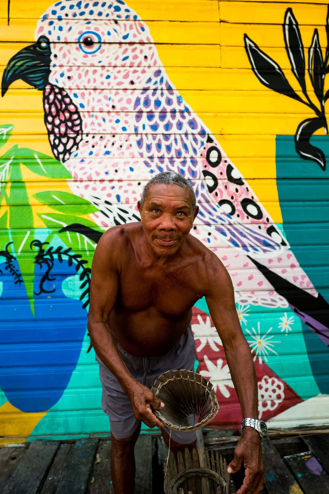 Morador segura um paneiro diante de um mural de pássaro