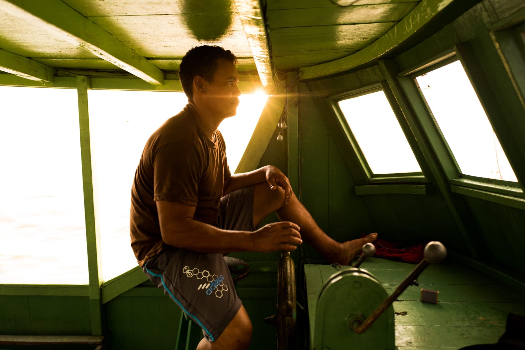 Rapaz pilota o barco com a luz do sol entrando pela janela