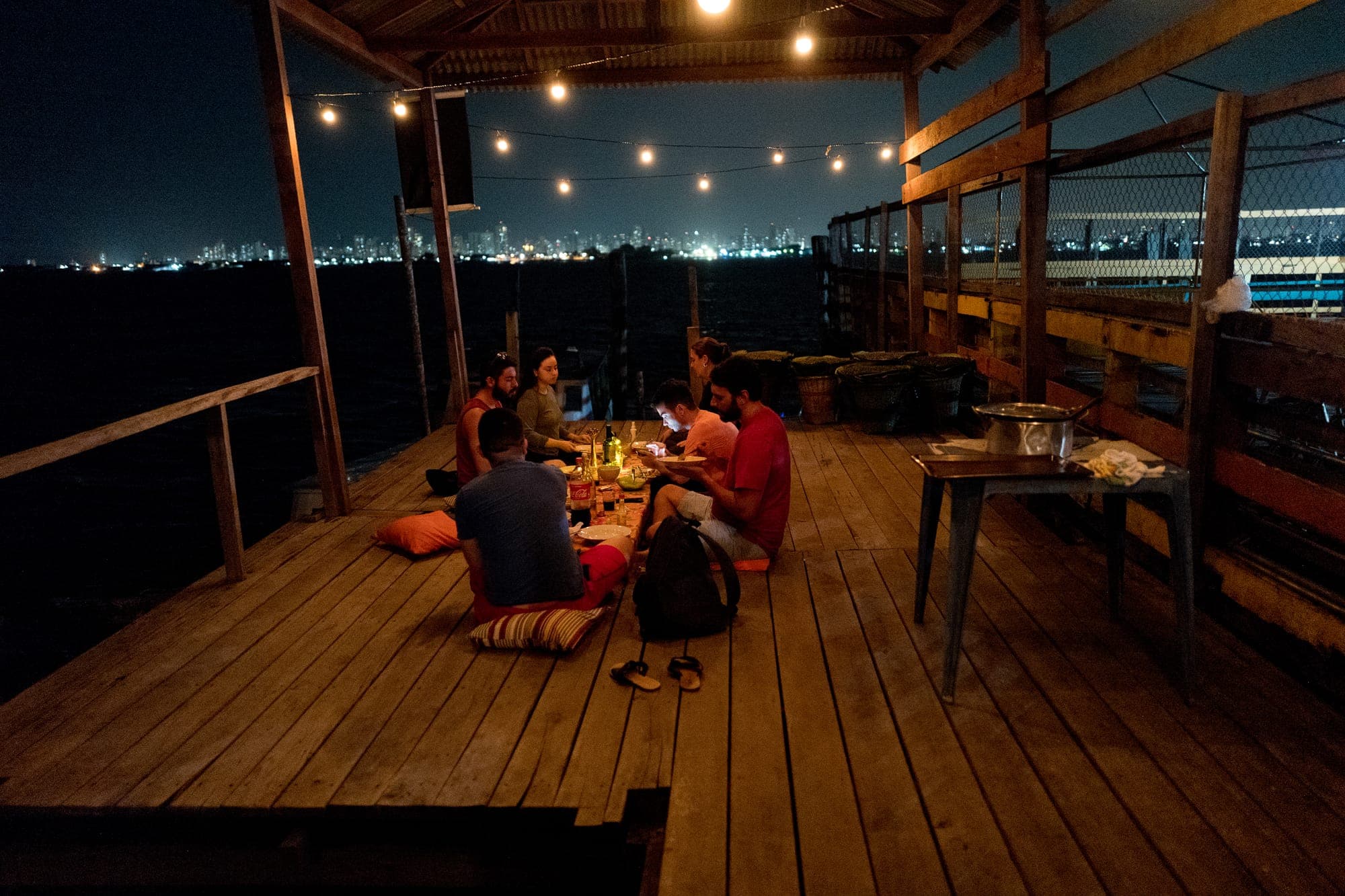 Grupo jantando no deck iluminado, com a cidade ao fundo