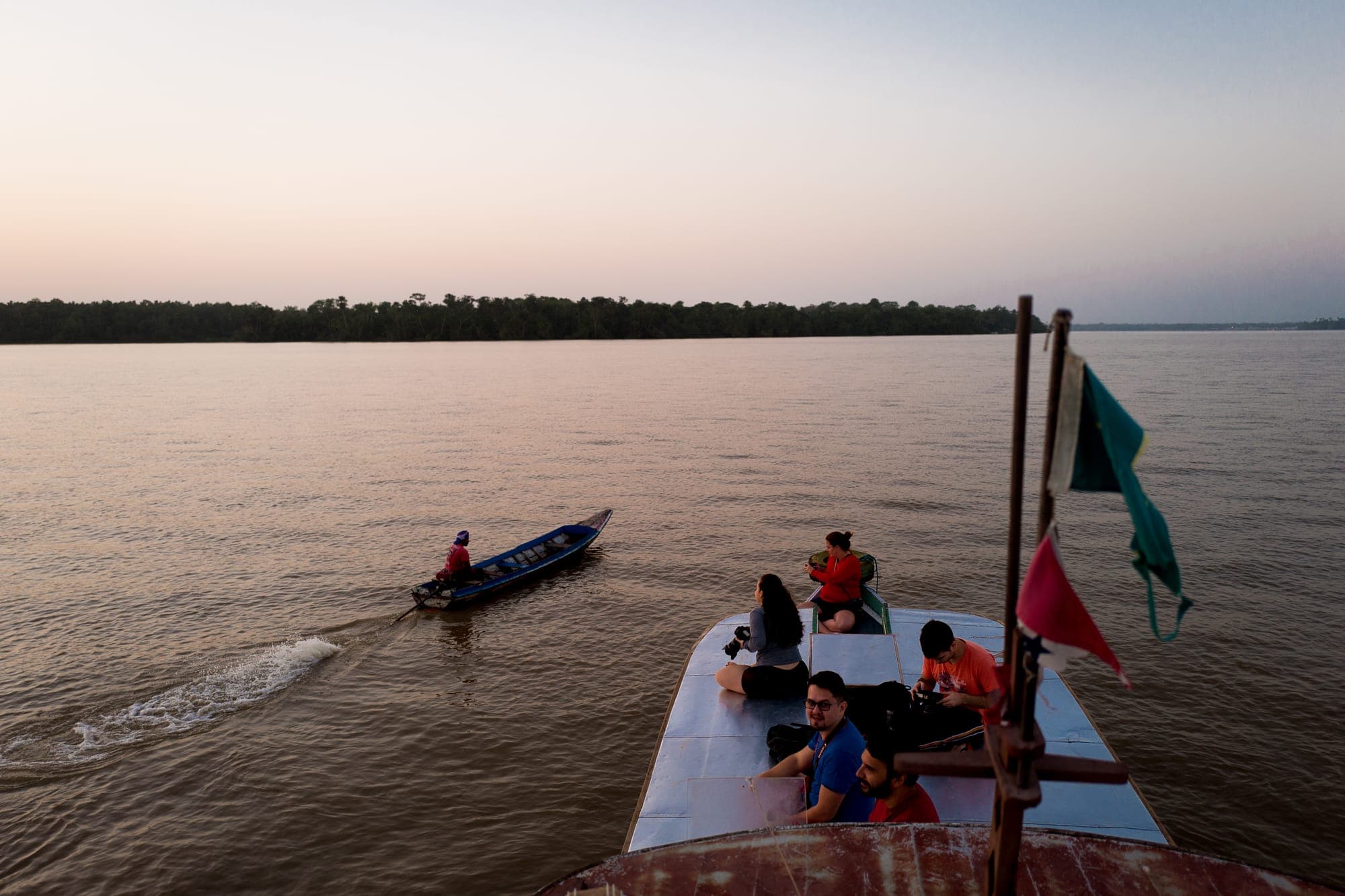 Participantes no teto do barco navegando no rio ao entardecer