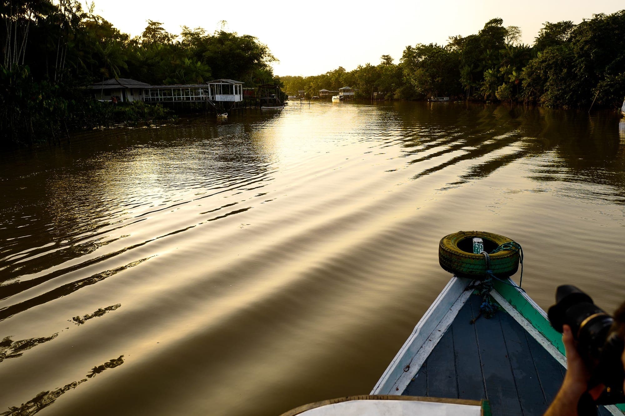 Proa do barco navegando pelo rio ao pôr do sol