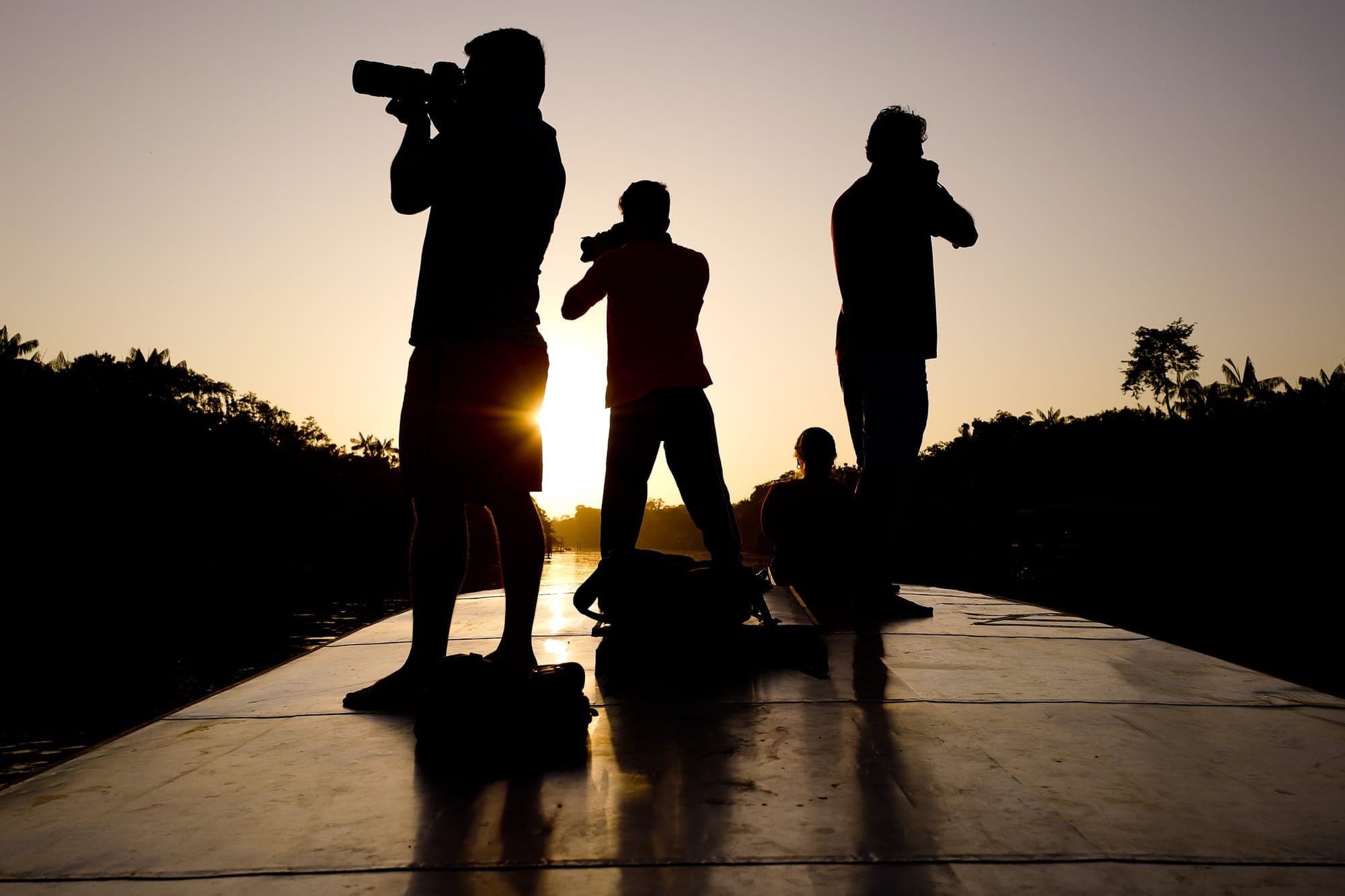 Silhuetas de três fotógrafos no barco contra o sol