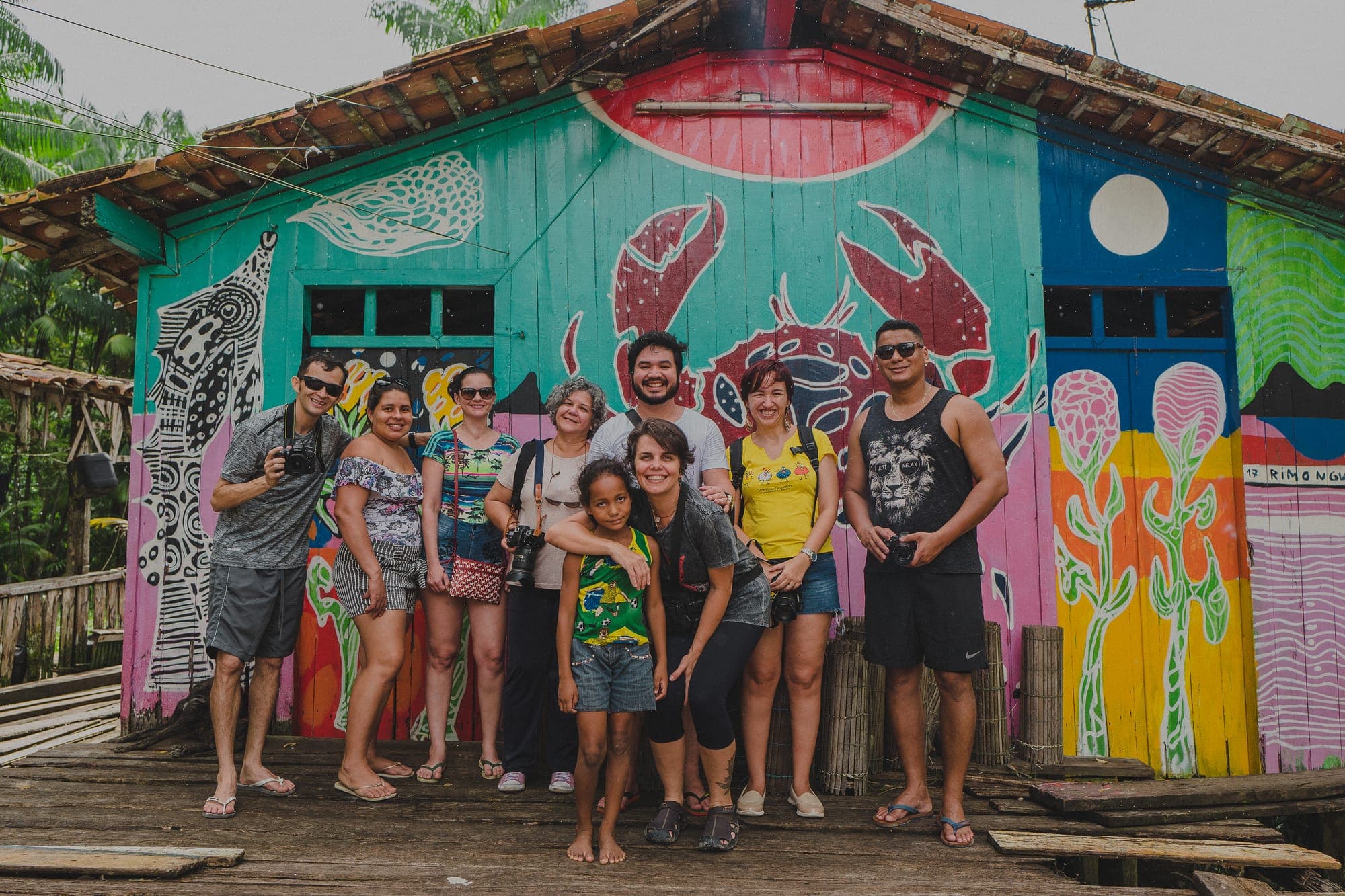 Grupo posa diante de uma casa pintada com murais