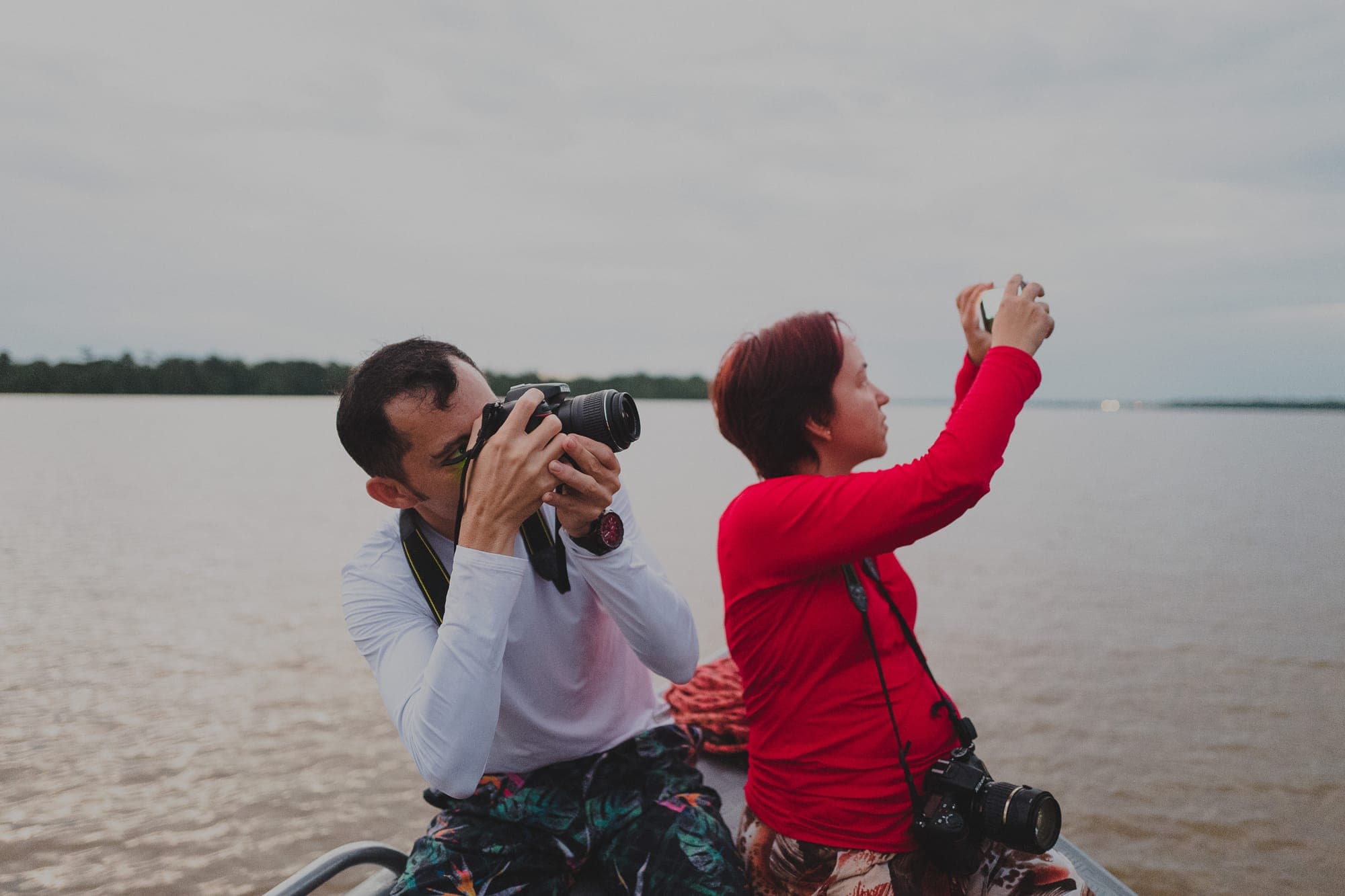 Dois participantes fotografam no barco, com o rio ao fundo